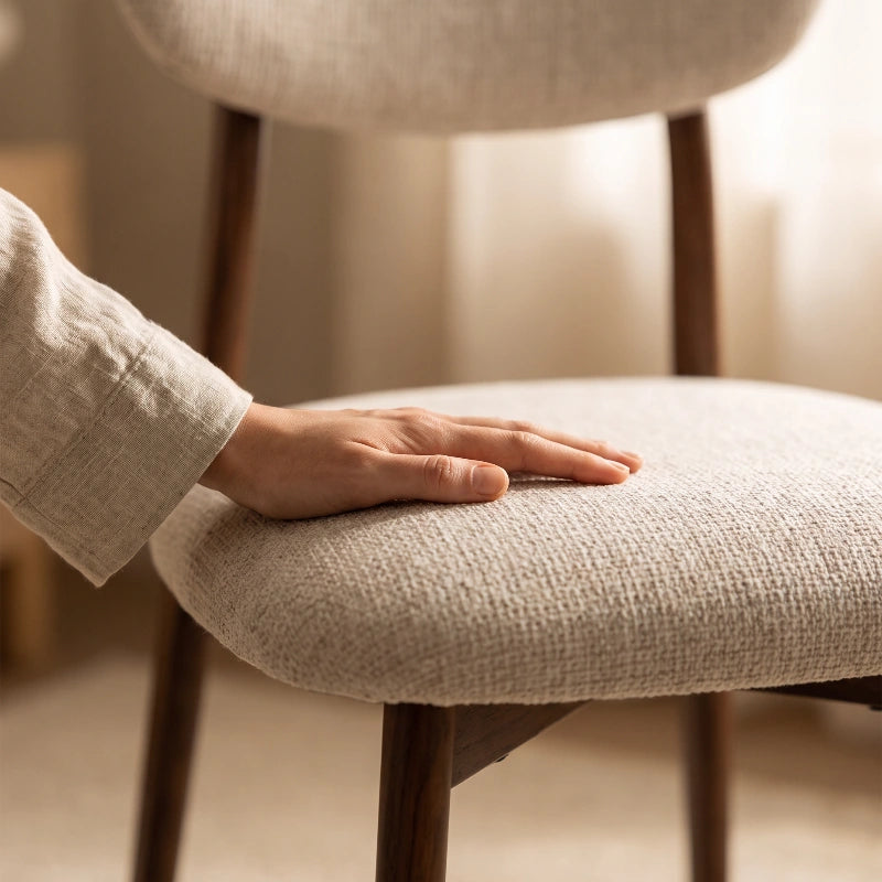 Close-up of a hand resting on the padded woven-fabric seat of a Japandi dining chair