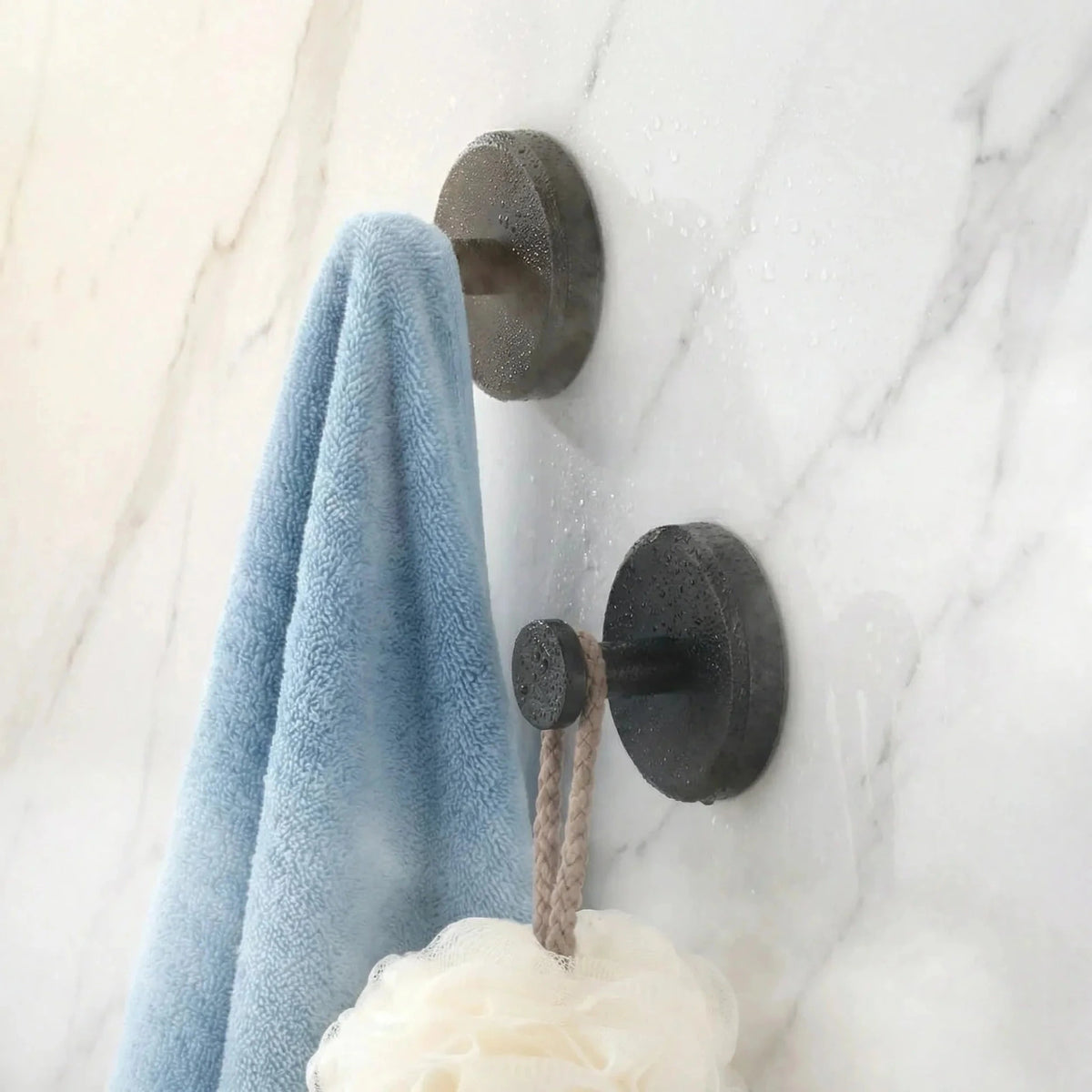 Black suction cup hooks holding a towel and bath sponge on smooth bathroom tiles