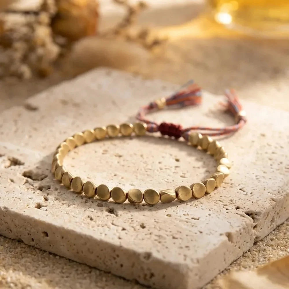 Copper and brass bead bracelet with an adjustable braided cord on a pale stone surface